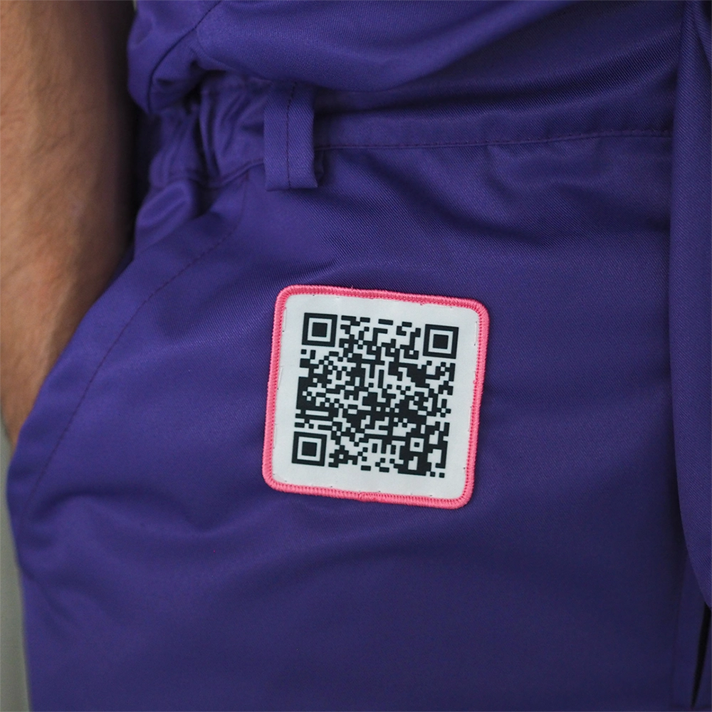 Painettu QR-koodi haalarimerkki, pinkki reuna, neliön muotoinen. Haalarimerkki ommeltuna violetteihin haalareihin.