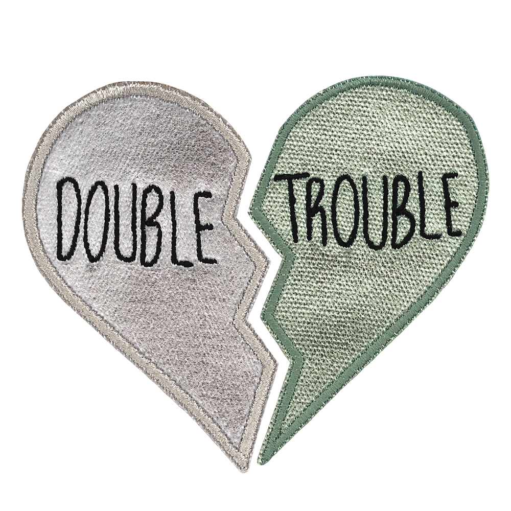 Metallinhohtoinen brodeerattu kaksiosainen haalarimerkki, merkeissä tekstit: Double ja Trouble.