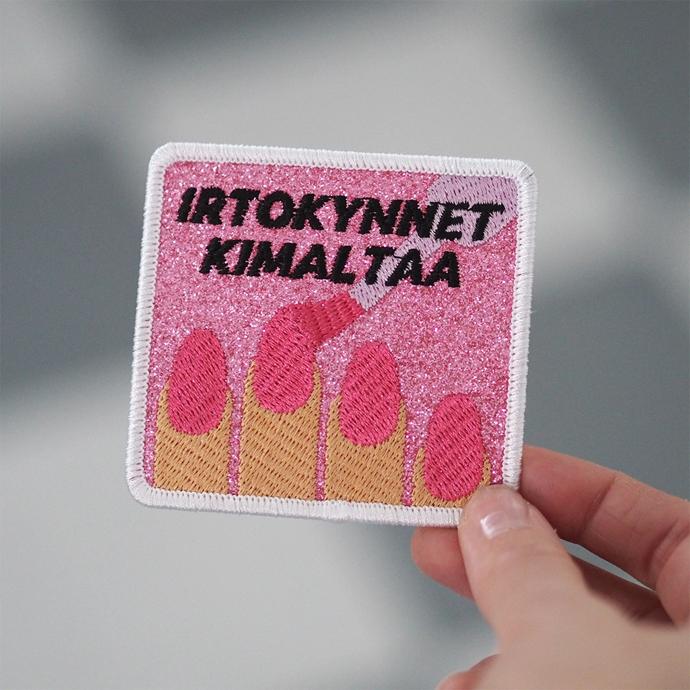 Brodeerattu merkki glitterkankaalla, kynsilakkaa, teksti: Irtokynnet kimaltaa.