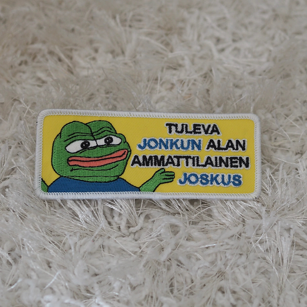 Brodeerattu Apustaja-haalarimerkki, teksti: Tuleva jonkun alan ammattilainen joskus. Merkki maton päällä.