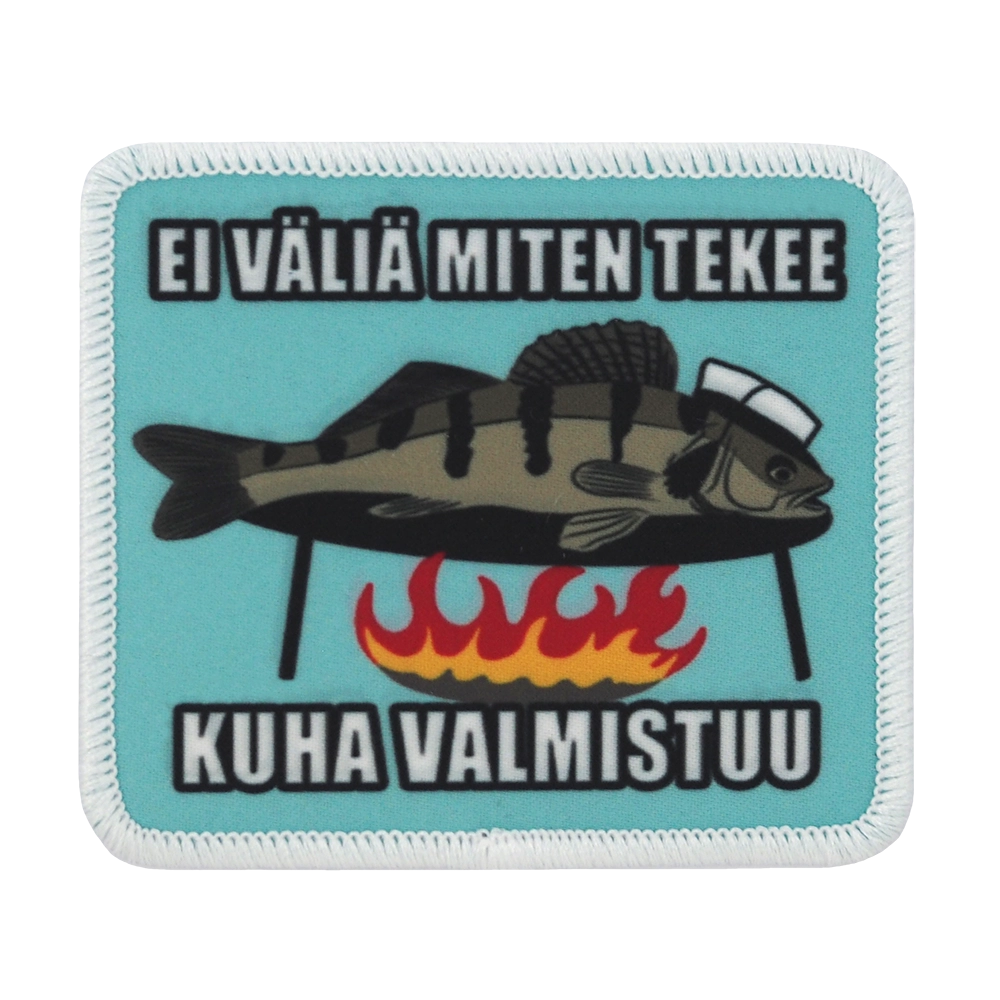 Painettu haalarimerkki, kuha nuotiolla, teksti: Ei väliä miten tekee kuha valmistuu.