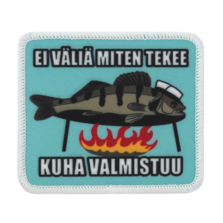 Painettu haalarimerkki, kuha nuotiolla, teksti: Ei väliä miten tekee kuha valmistuu.