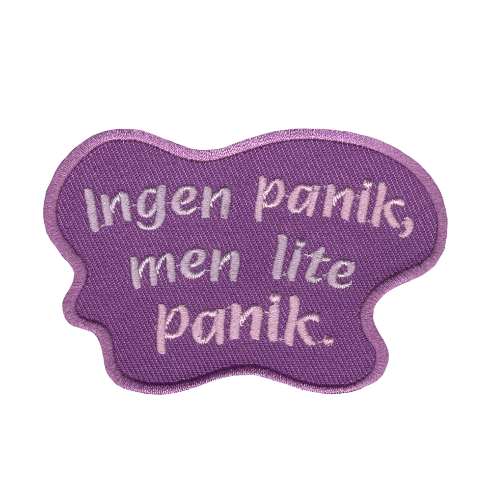 Brodeerattu kangasmerkki, teksti: Ingen panik, men lite panik.