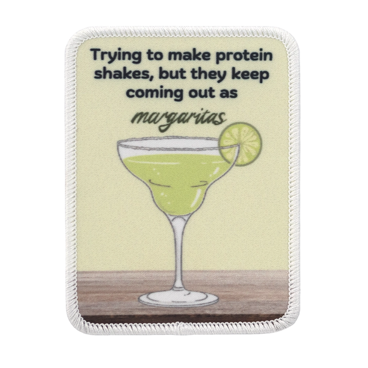 Painettu margarita-aiheinen haalarimerkki, teksti: Trying to make protein shakes, but they keep coming out as margaritas.