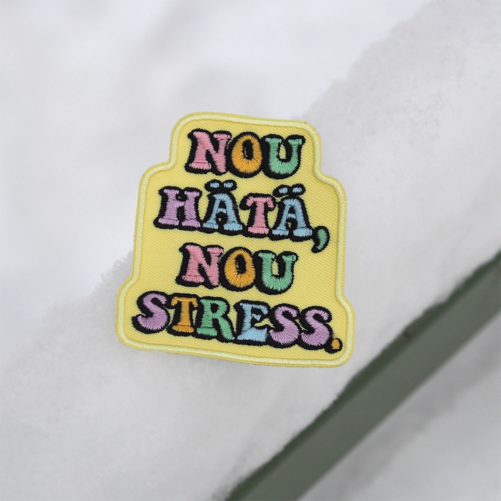 Brodeerattu haalarimerkki, keltainen, teksti: Nou hätä, nou stress. Merkki lumella.