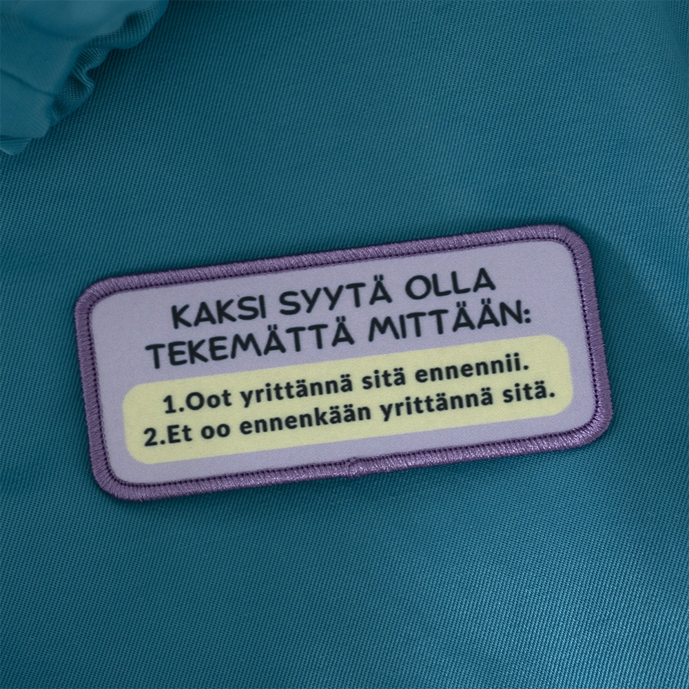 Painettu merkki, savolainen, yrittännä. Taustalla opiskelijahaalarit.