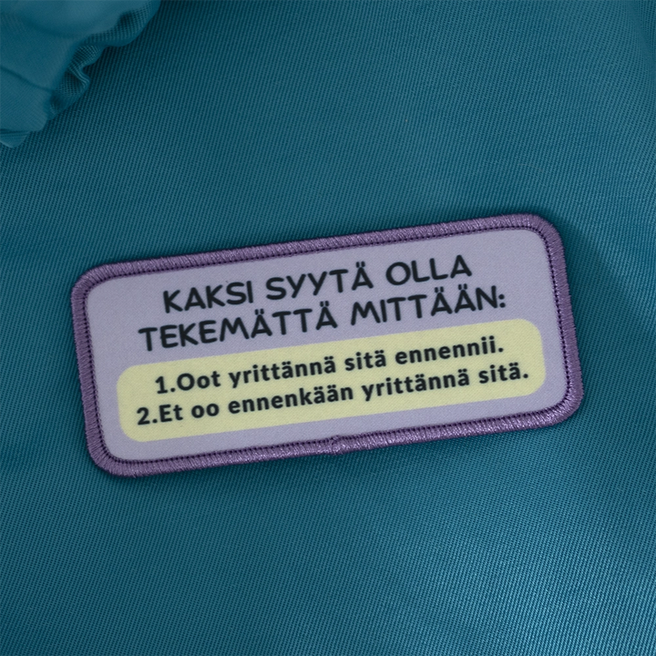 Painettu merkki, savolainen, yrittännä. Taustalla opiskelijahaalarit.